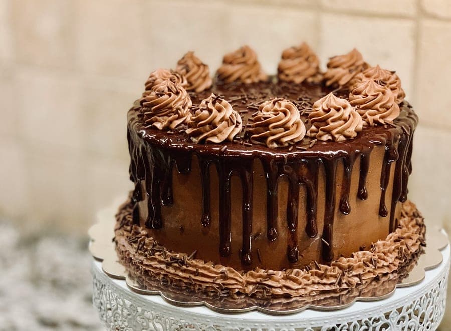 Chocolate drip cake with piped swirls on a cake stand